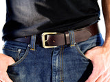 Brown leather belt with a gold roller buckle worn with blue jeans.