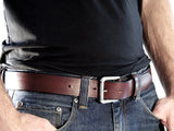 Cognac brown leather belt with a removable silver buckle and a belt loop, worn with blue jeans and a black shirt.