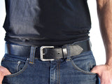 Black leather belt with silver roller buckle worn with jeans.